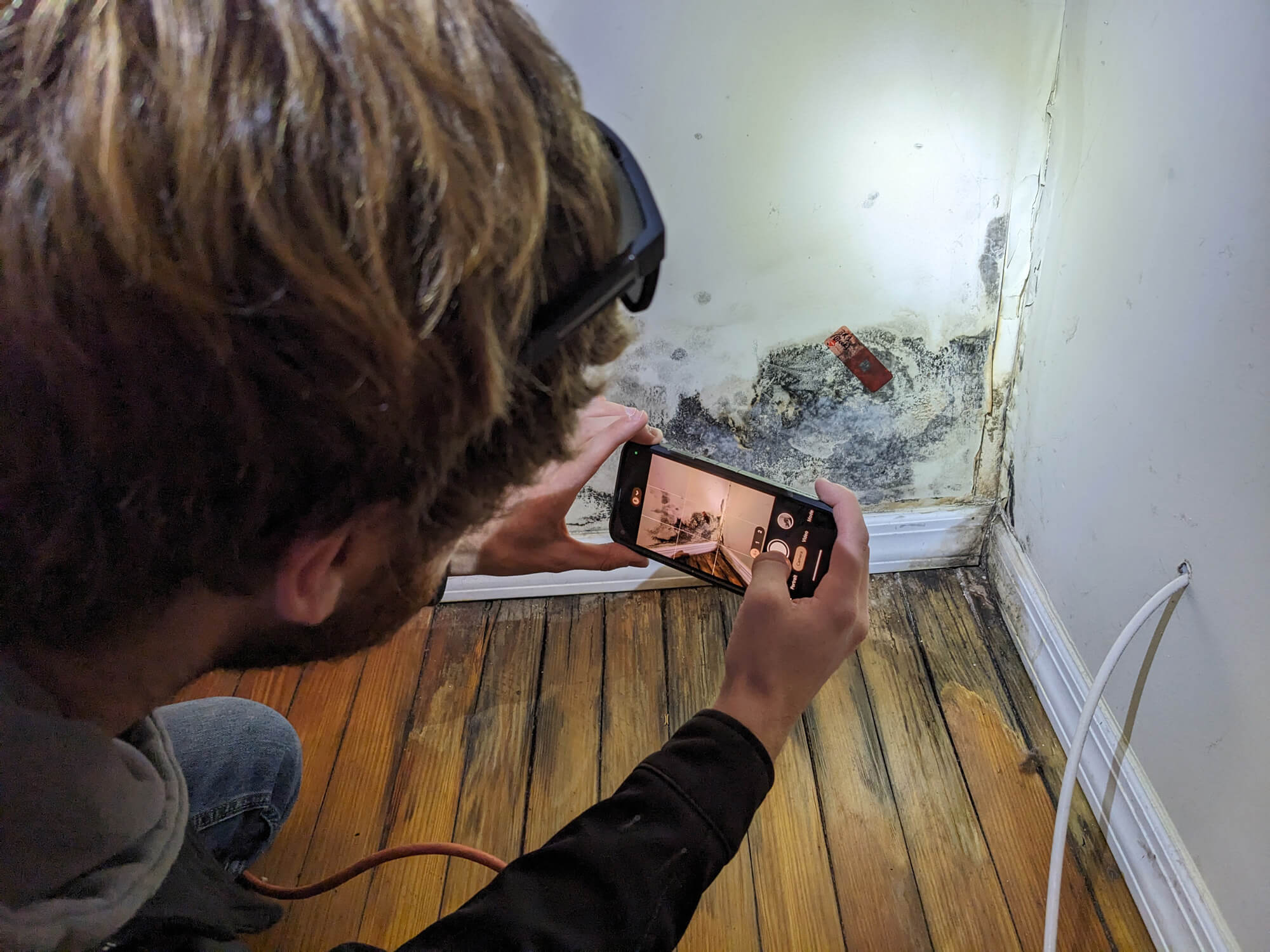 A professional uses a phone to photograph a mold tape lift sample on a ceiling for laboratory analysis.