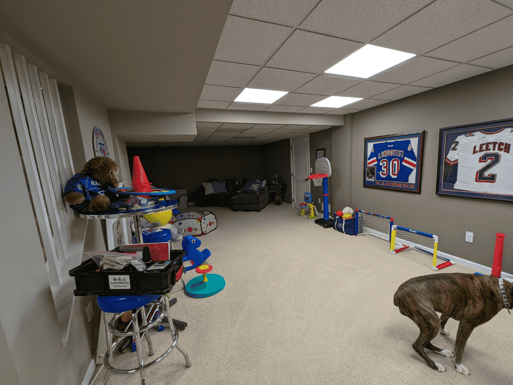 Finished basement playroom with clean carpeting and framed sports jerseys after environmental remediation.