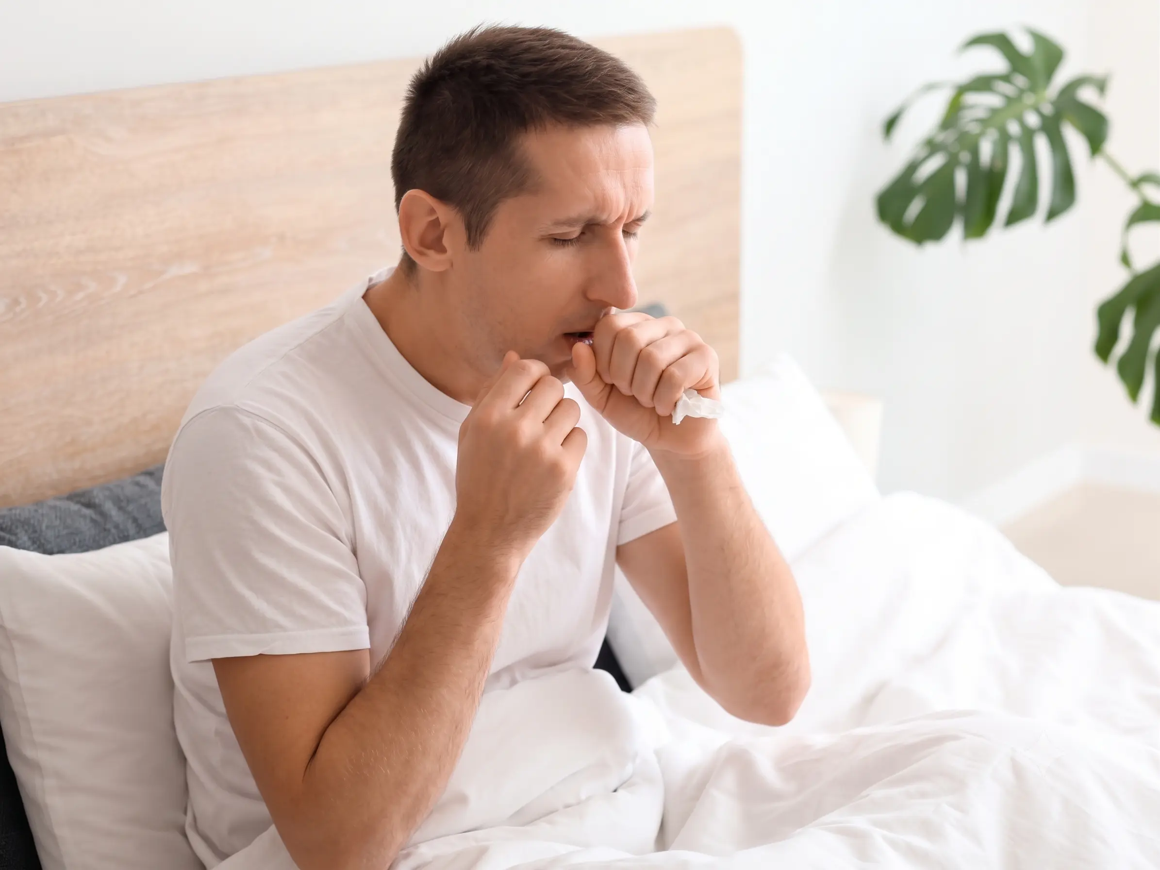 Man resting in bed coughing from indoor environmental triggers and mold exposure, illustrating symptoms of environmentally acquired illness.